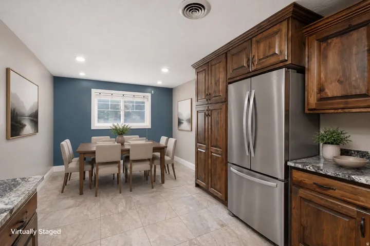 Combined kitchen and dining area featuring wood-finish cabinetry, stainless steel refrigerator, granite-style countertops, recessed ceiling lighting, and large format floor tiling