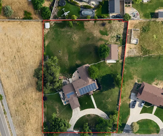 Expansive property featuring a primary residence with solar panels, a separate auxiliary structure, a circular driveway, mature trees, and a substantial undeveloped rear parcel