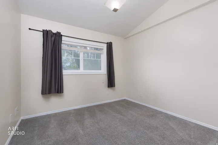 Carpeted room featuring a window with white trim, a dark curtain rod, and a vaulted ceiling