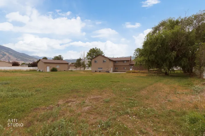 Expansive grassy area with mountain backdrop, featuring a detached two-story residence with multiple windows and a separate accessory structure