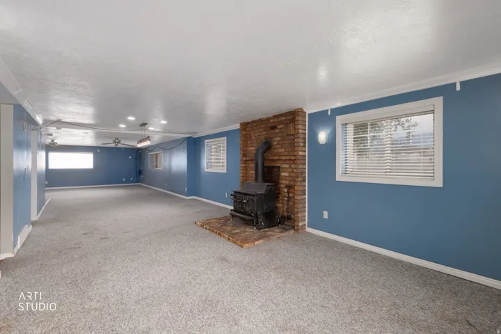 Spacious room featuring a brick wood-burning stove, light-toned carpeting, multiple windows with blinds, and white crown molding