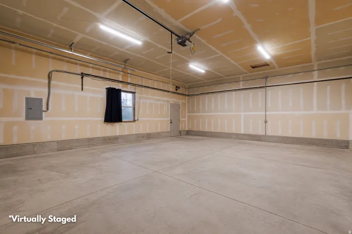 Spacious garage featuring concrete flooring, exposed drywall, multiple fluorescent light fixtures, and a side window