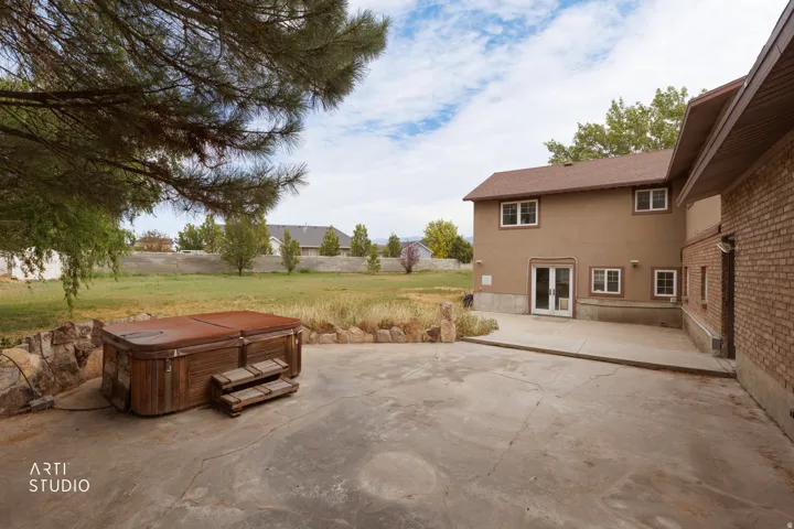 Expansive concrete patio featuring a built-in hot tub with wood-finish siding and steps