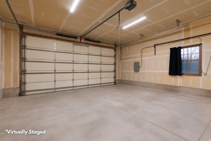 Spacious garage featuring a concrete floor, overhead lighting, an automatic garage door opener, and a window with a dark curtain
