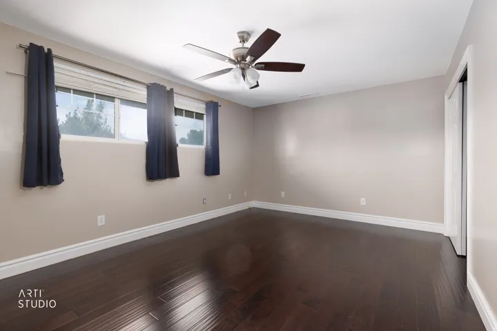 Spacious room featuring dark wood-finish flooring, light-colored walls, crown molding, and a ceiling fan with integrated lighting