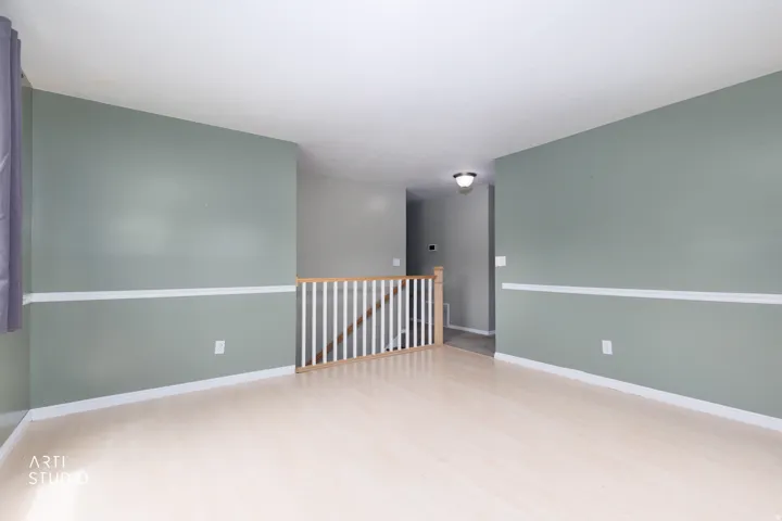 Open living area featuring light wood-finish flooring, light green walls with white chair rail molding, and a white ceiling