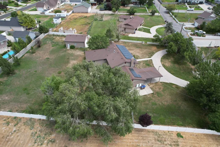 Expansive property featuring a brown-roofed residence with solar panels, a detached outbuilding, mature trees, and a curved paved driveway