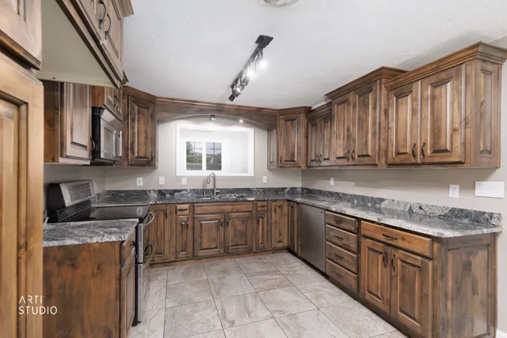Spacious kitchen featuring extensive wood cabinetry, stone countertops, stainless steel appliances, and tile flooring