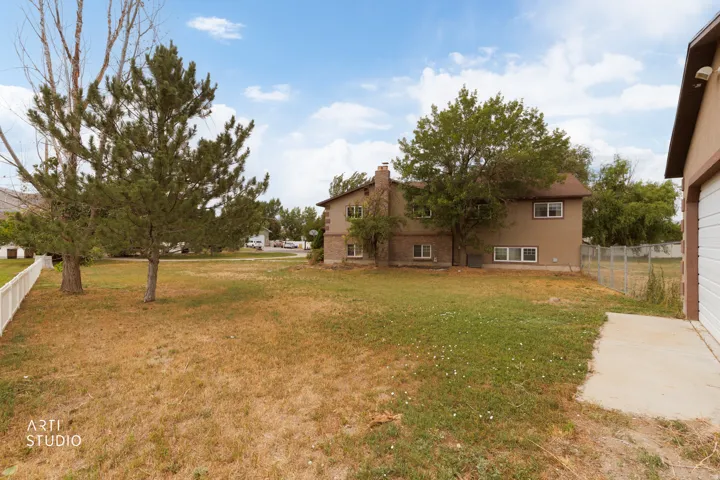 Spacious rear yard featuring mature trees, a white picket fence, and a concrete pad