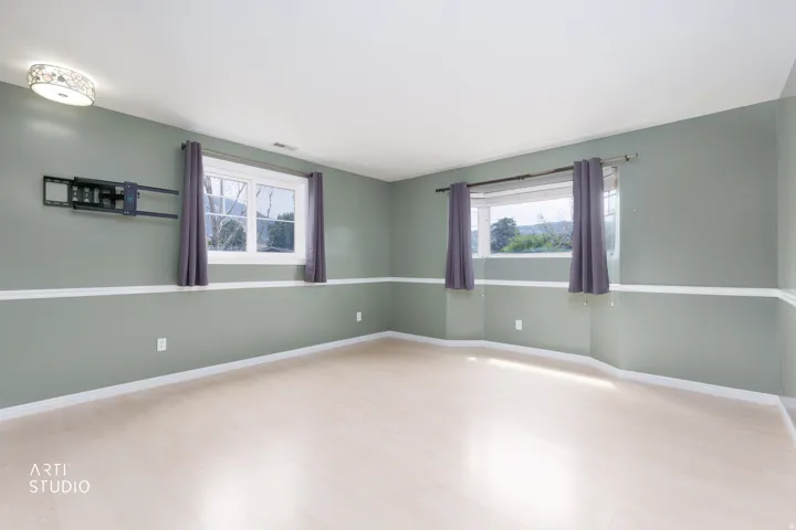 Spacious room featuring light-toned wood-finish flooring, two windows with white trim, and a decorative flush-mount ceiling light