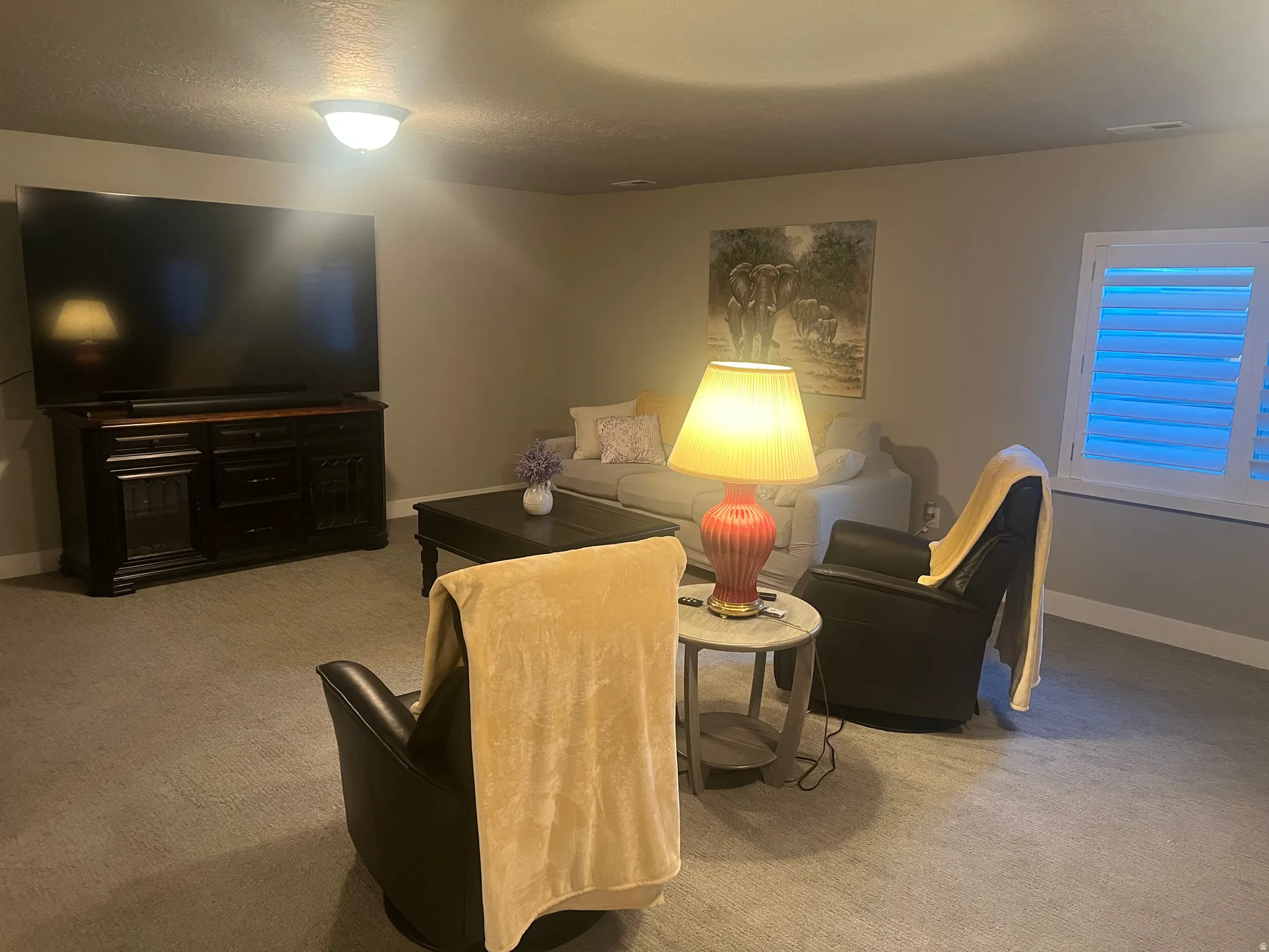 Spacious living area featuring neutral carpeting, recessed lighting, and a window with plantation shutters