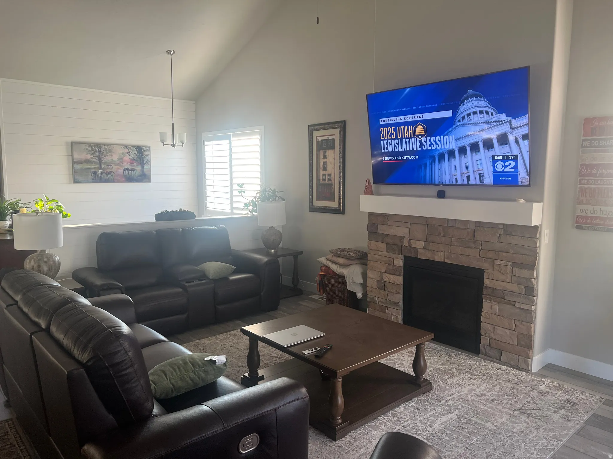 Vaulted ceiling living area featuring a stone-faced fireplace with a white mantel, shiplap accent wall, and wood-finish flooring