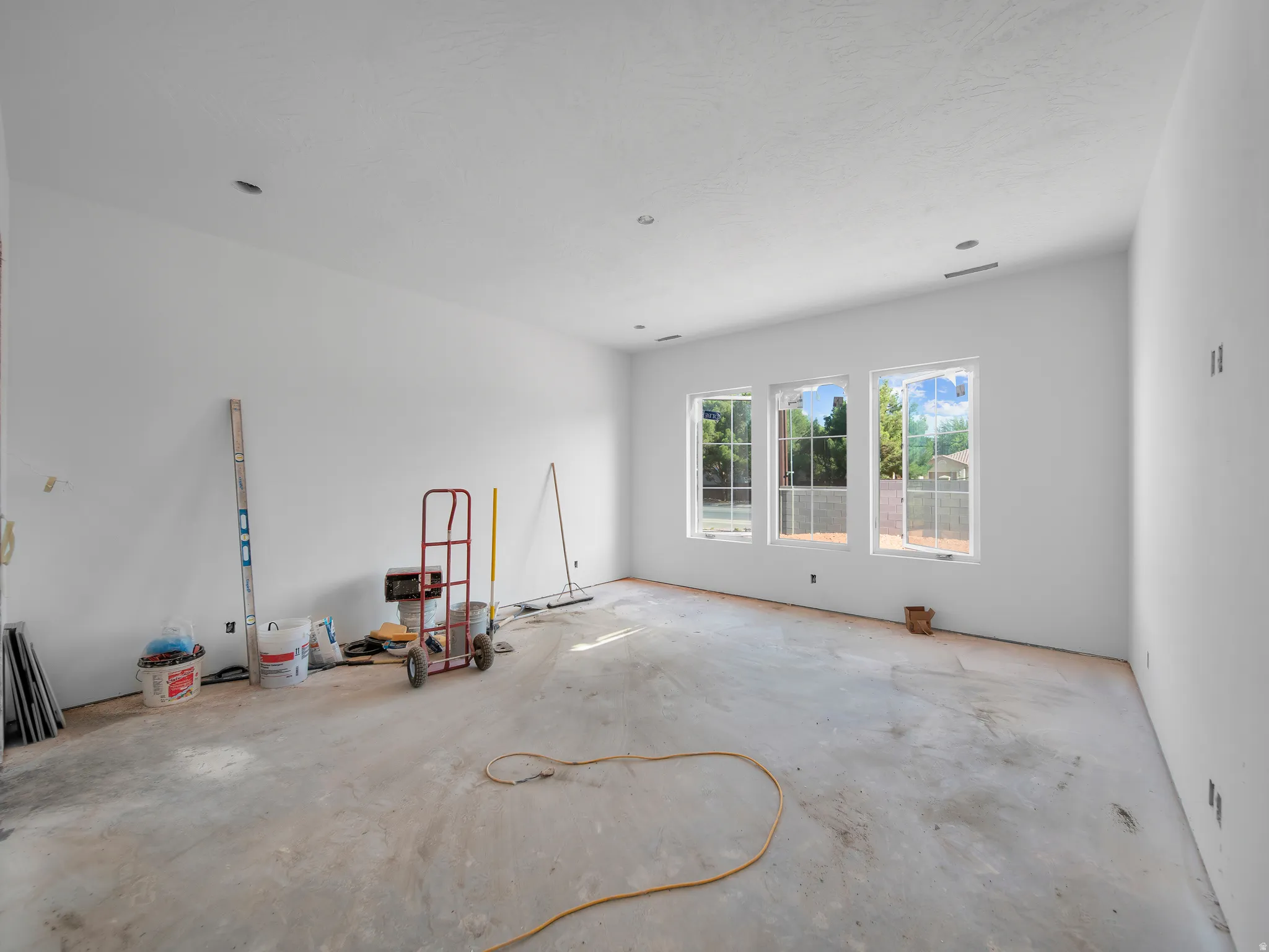 Spacious room featuring three large windows, white walls, and a textured ceiling
