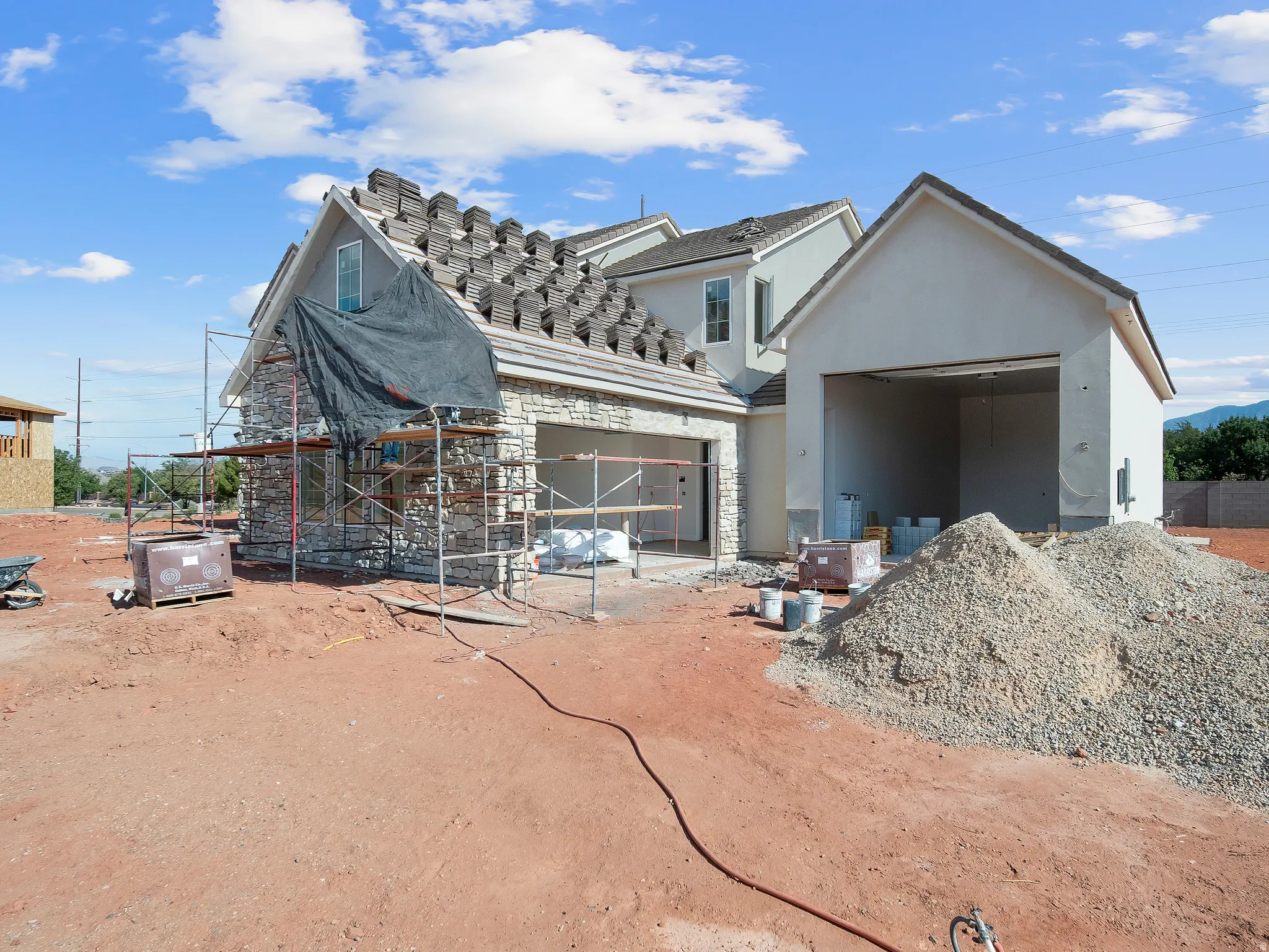 New construction home featuring a partial stone facade, stucco exterior, and multi-pitched roofline with installed tiles