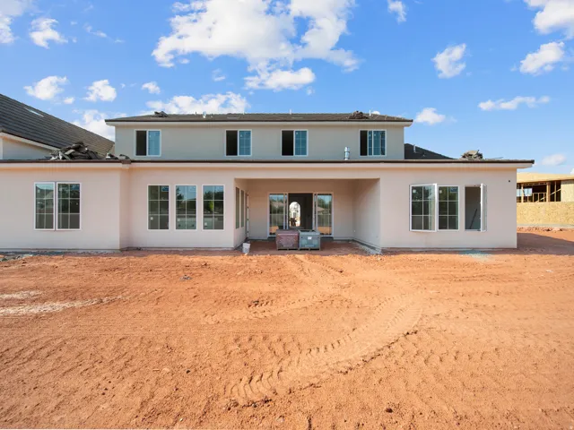 Rear exterior featuring an expansive dirt lot, a covered patio area, and multiple white-framed windows