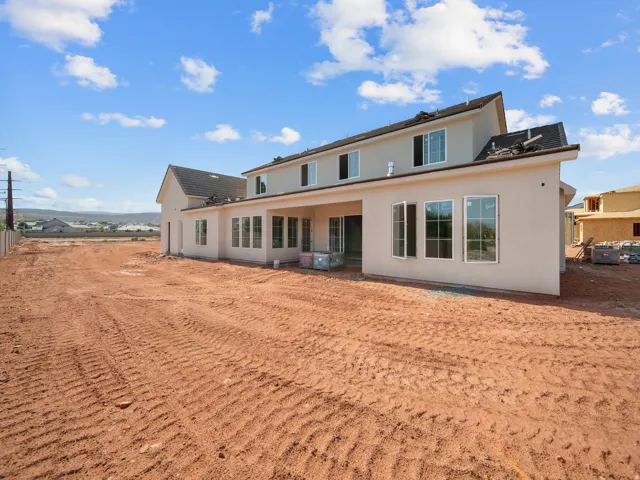 Rear exterior featuring a stucco finish, multiple windows, a sliding glass door, and a covered patio area