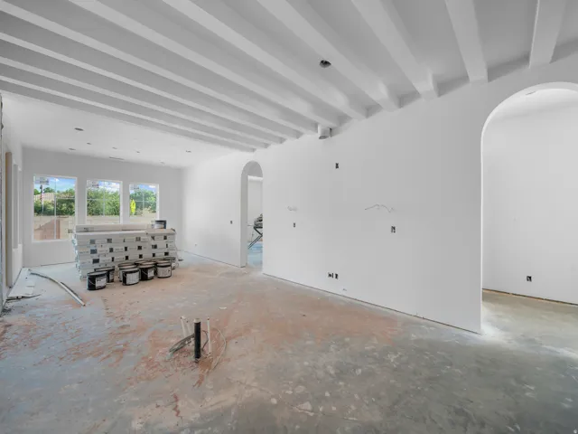 Spacious interior featuring a beamed ceiling, multiple large windows, and an arched doorway