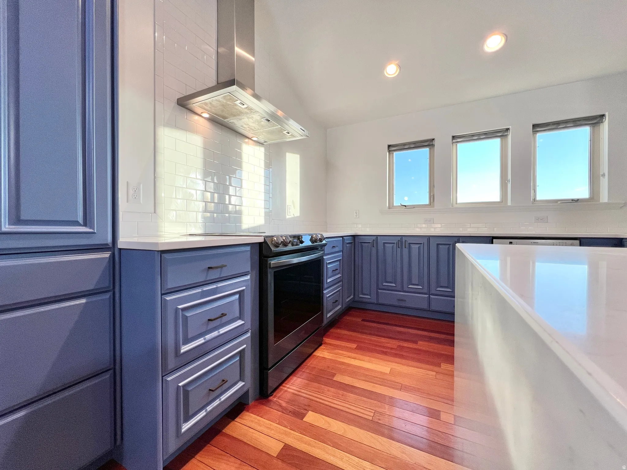 Kitchen featuring blue cabinetry, white countertops, wood-finish flooring, a stainless steel range hood, and a white subway tile backsplash