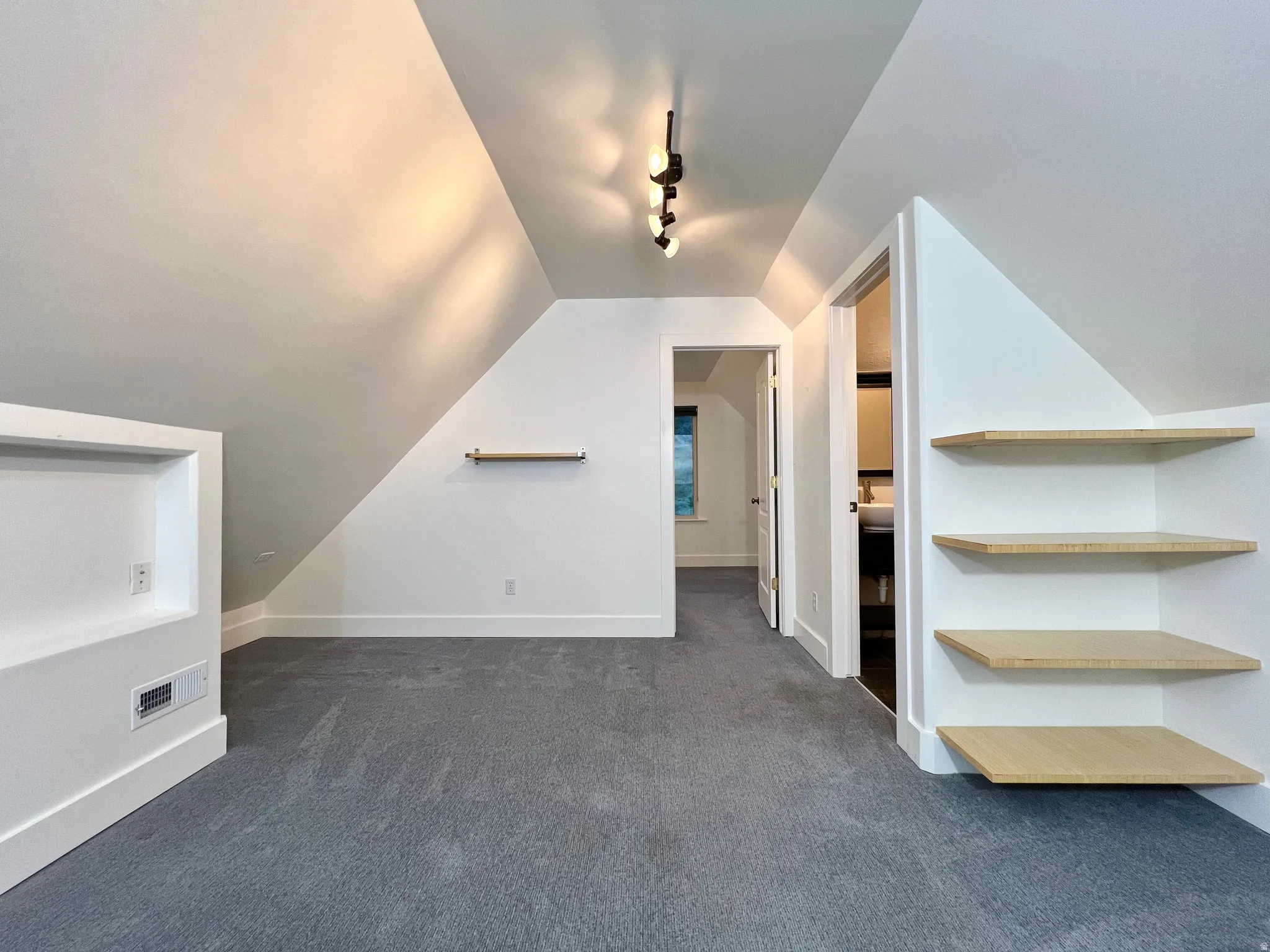 Carpeted space with sloped ceilings, track lighting, built-in shelving, and a recessed wall niche with an electrical outlet