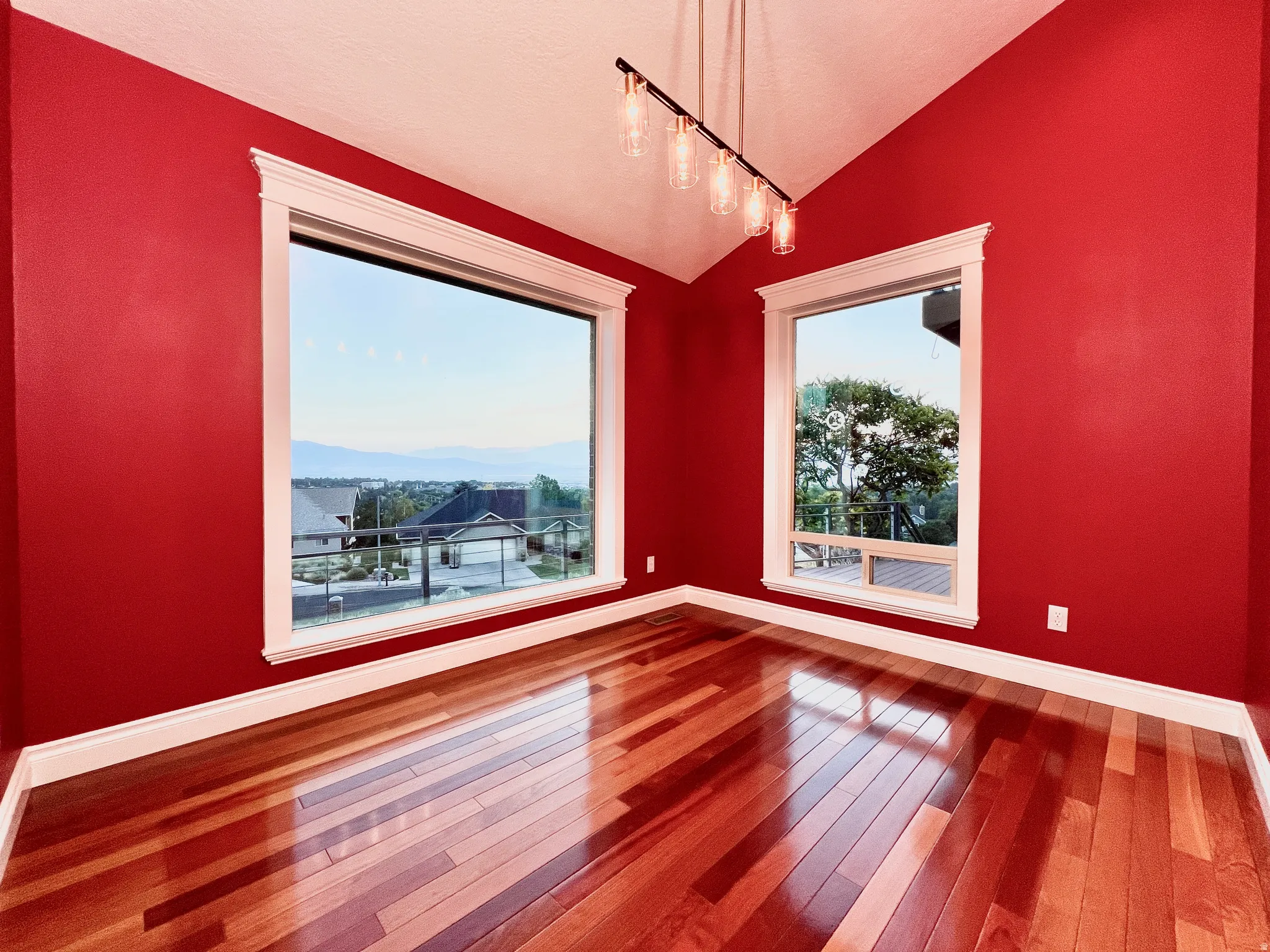 Spacious room featuring vaulted ceilings, rich wood-finish flooring, and large windows with white trim