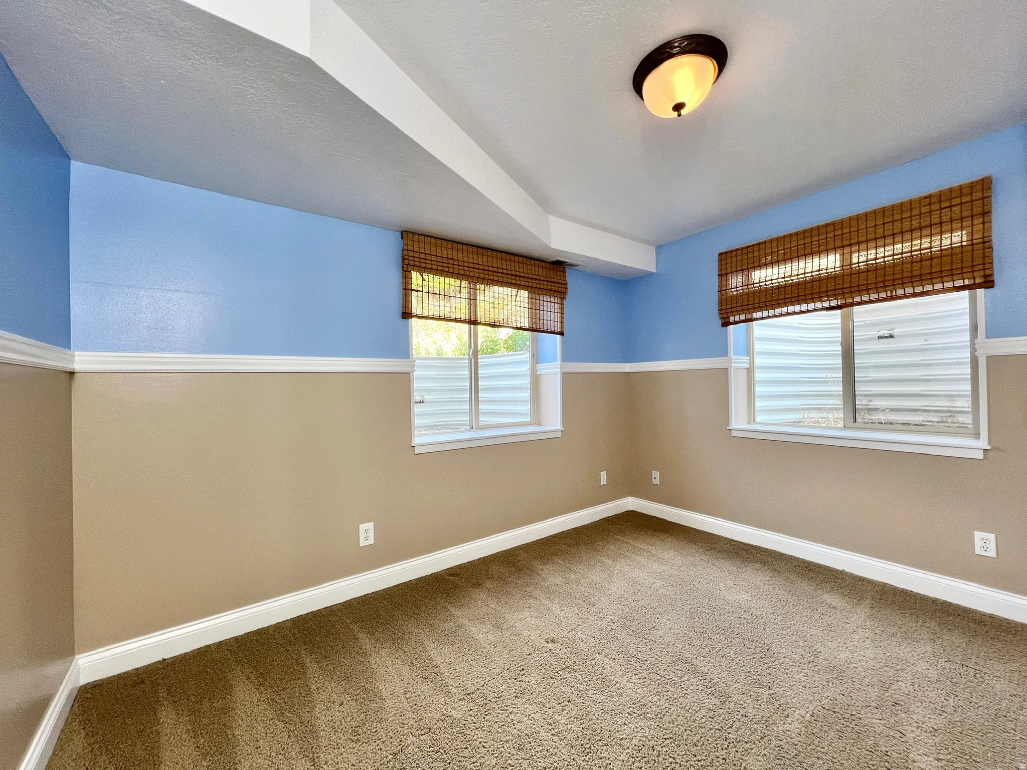 Carpeted room featuring two-tone wall paint, white trim, and two windows with bamboo blinds