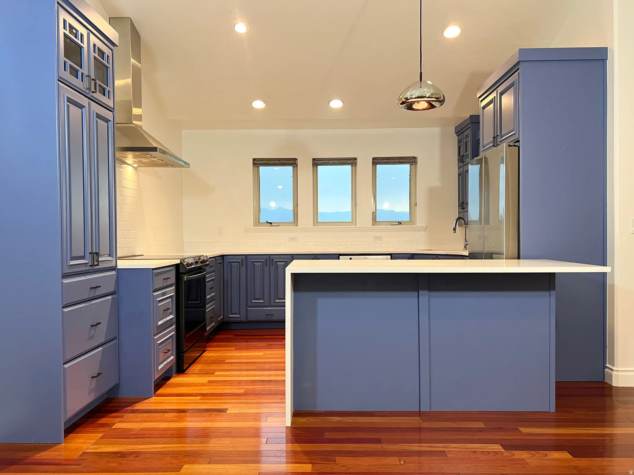 Kitchen featuring blue shaker-style cabinetry, a built-in stainless steel range hood, white countertops, and wood-finish flooring