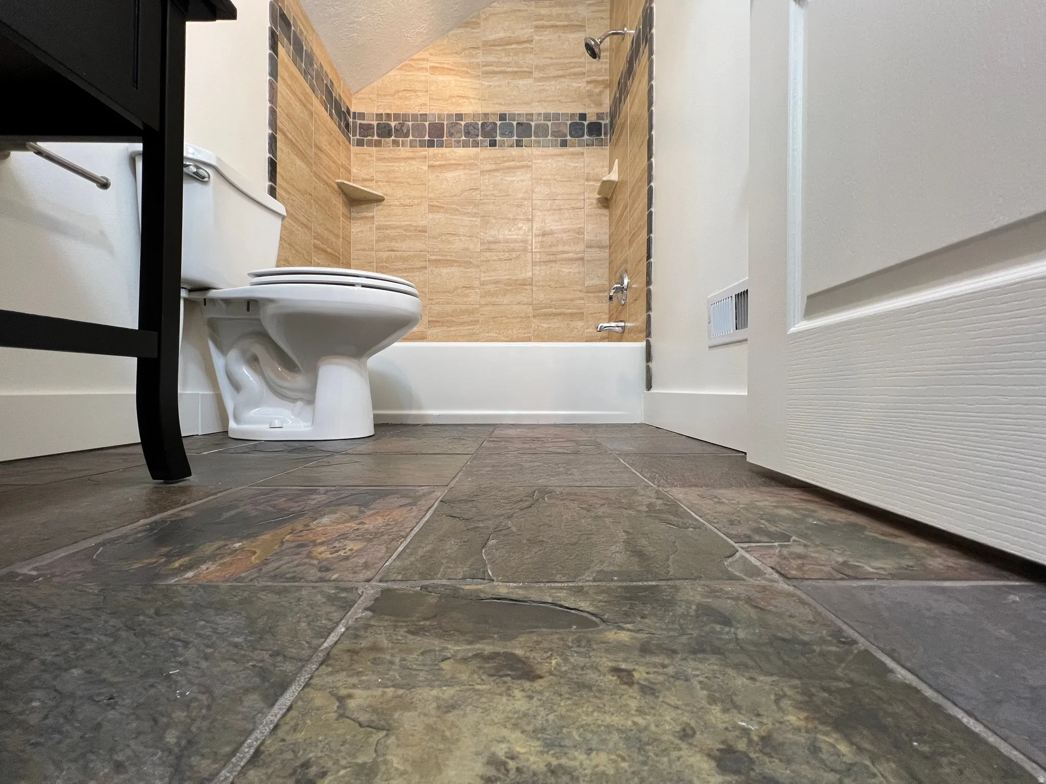 Bathroom featuring large format slate-look floor tiles, a standard toilet, and a bathtub with beige subway tile surround