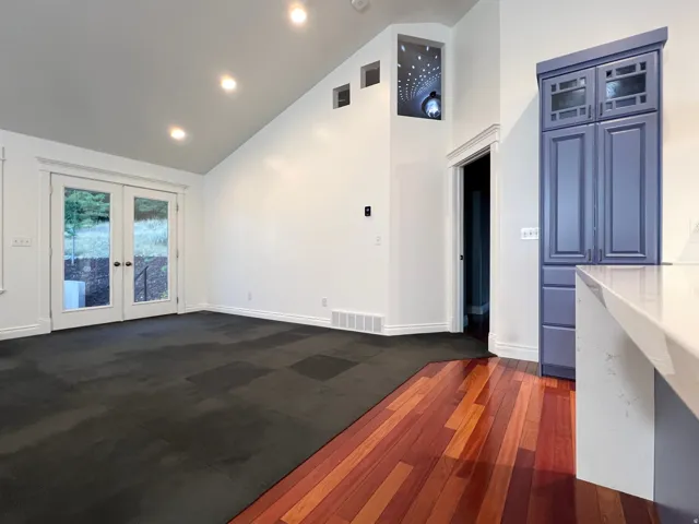 Vast open-concept space featuring a vaulted ceiling with recessed lighting, French doors, and contrasting flooring