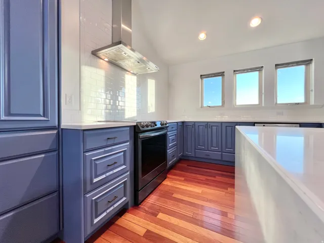 Kitchen featuring blue cabinetry, white countertops, wood-finish flooring, a stainless steel range hood, and a white subway tile backsplash