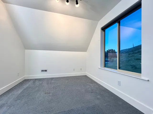 Attic room with angled ceilings, track lighting, and a large window offering natural light and scenery