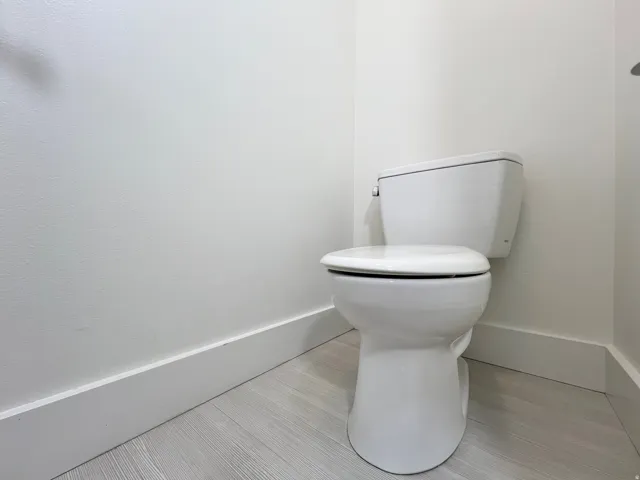 White ceramic toilet in a room featuring light wood-finish flooring, white painted walls, and white baseboard trim