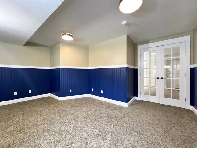 Room featuring carpet flooring, blue wainscoting, light beige painted walls, and white trim