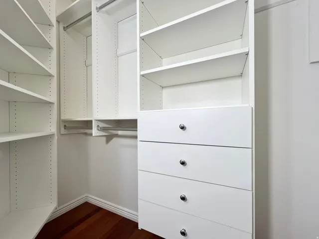 Custom closet system featuring white shelving, multiple hanging rods, built-in drawers with chrome hardware, and wood-finish flooring