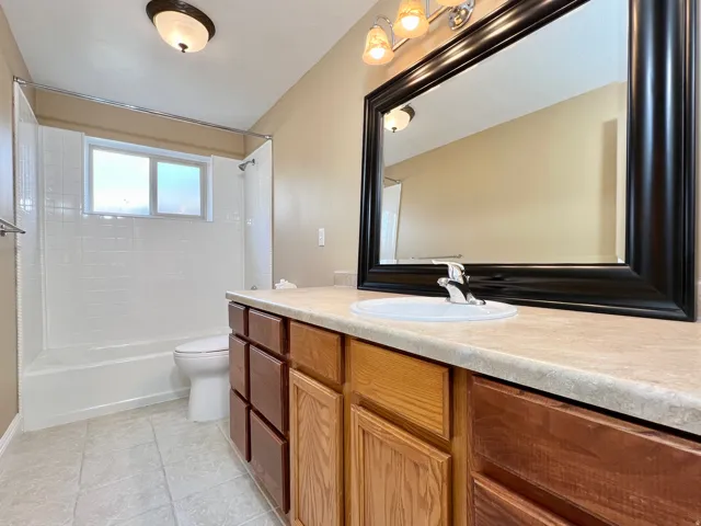 Bathroom featuring a wood-finish vanity with a light-toned countertop, an integrated sink, and a large black-framed mirror