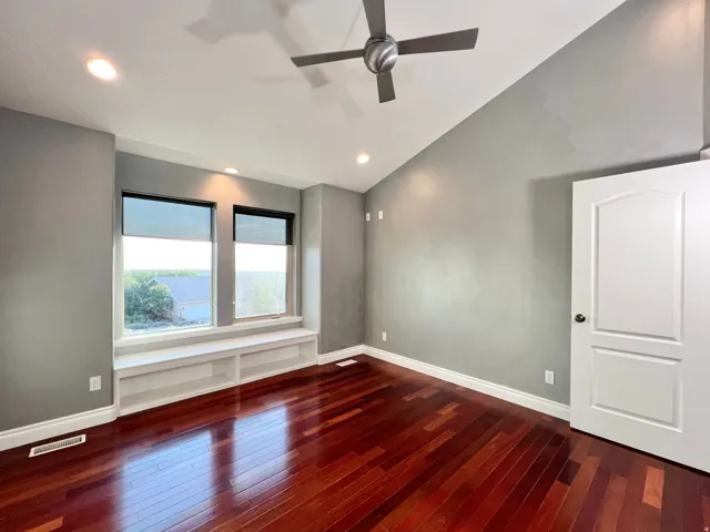 Spacious room featuring rich wood-finish flooring, a built-in window bench with integrated shelving, recessed lighting, a modern ceiling fan, and a paneled interior door