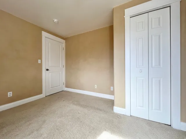Carpeted interior space featuring neutral tone walls, white trim, a bi-fold closet door, and a paneled entry door