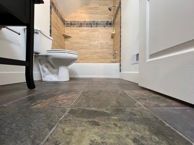 Bathroom featuring large format slate-look floor tiles, a standard toilet, and a bathtub with beige subway tile surround