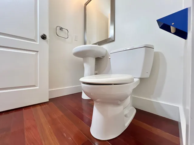 Powder room featuring a white pedestal sink, white toilet, and wood-finish flooring