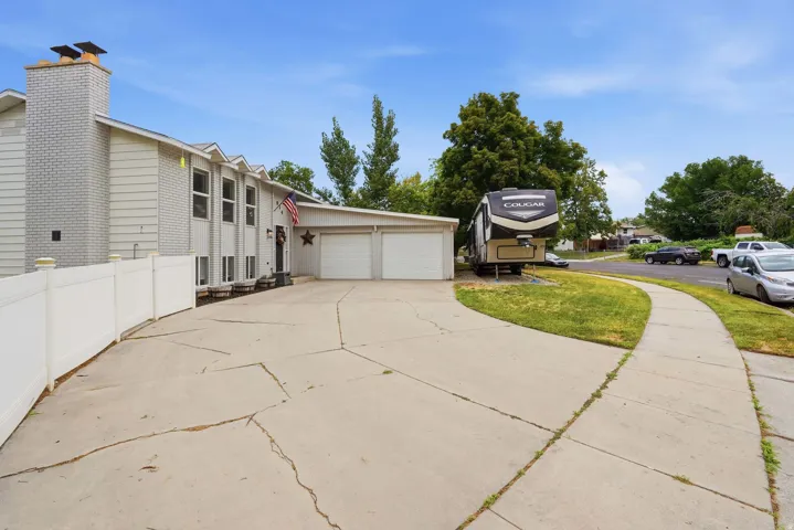 Exterior showcasing a two-car garage, expansive concrete driveway, and white privacy fencing