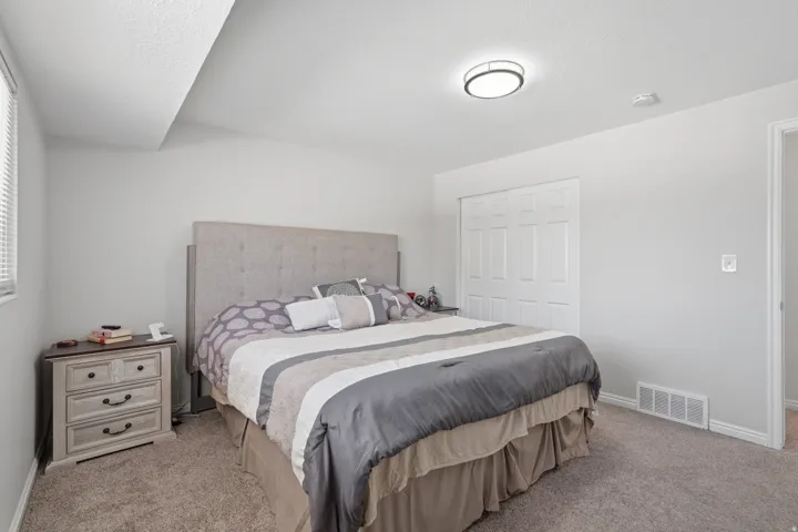 Carpeted room featuring a light gray upholstered headboard, white bi-fold closet doors, and a ceiling-mounted light fixture