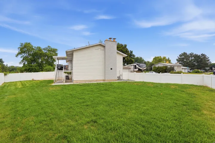 Expansive green lawn surrounds the home, bordered by a white vinyl privacy fence