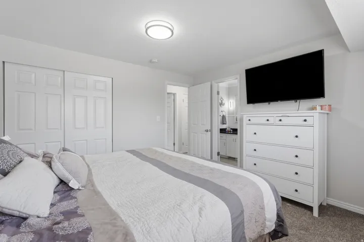 Carpeted bedroom featuring a flat-panel ceiling light, sliding closet doors, and an en-suite bathroom entry