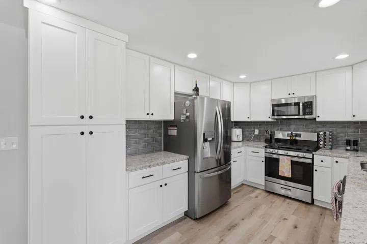 Modern kitchen featuring white shaker cabinetry, stainless steel appliances, speckled stone countertops, a gray subway tile backsplash, and light wood-finish flooring