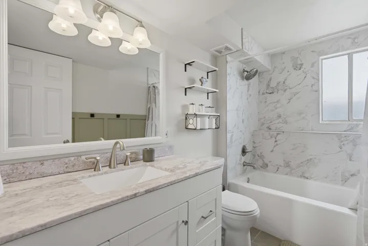 Contemporary bathroom featuring a white vanity with a light-colored countertop, brushed nickel fixtures, a built-in bathtub, and marble-patterned shower tiling extending to the ceiling
