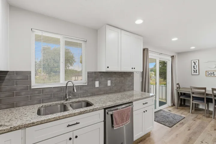 Kitchen featuring a double basin stainless steel sink, granite-style countertops, white shaker cabinetry with dark hardware, and a gray subway tile backsplash