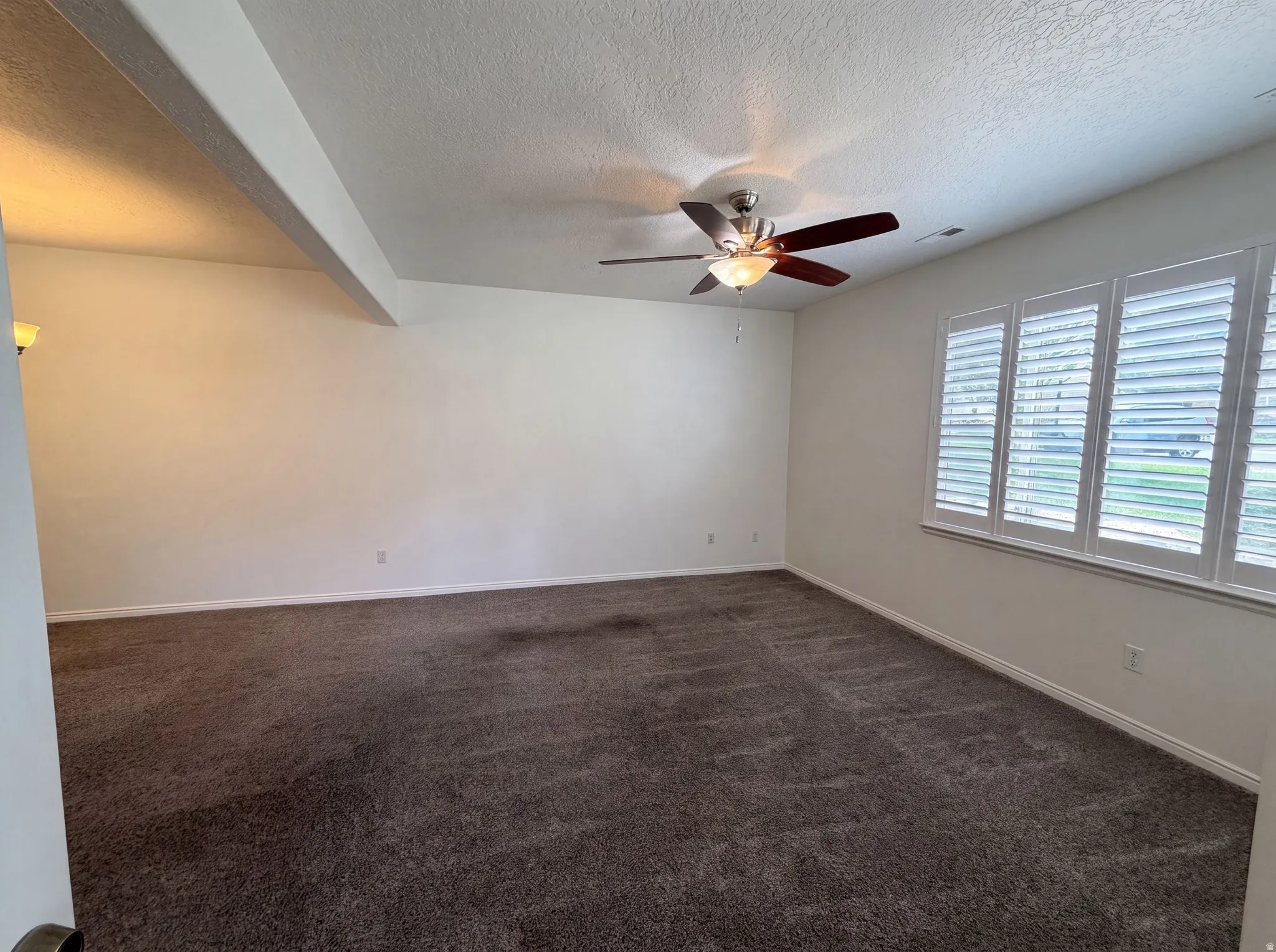 Carpeted room with a ceiling fan, three windows featuring white plantation shutters, and a wall-mounted light fixture
