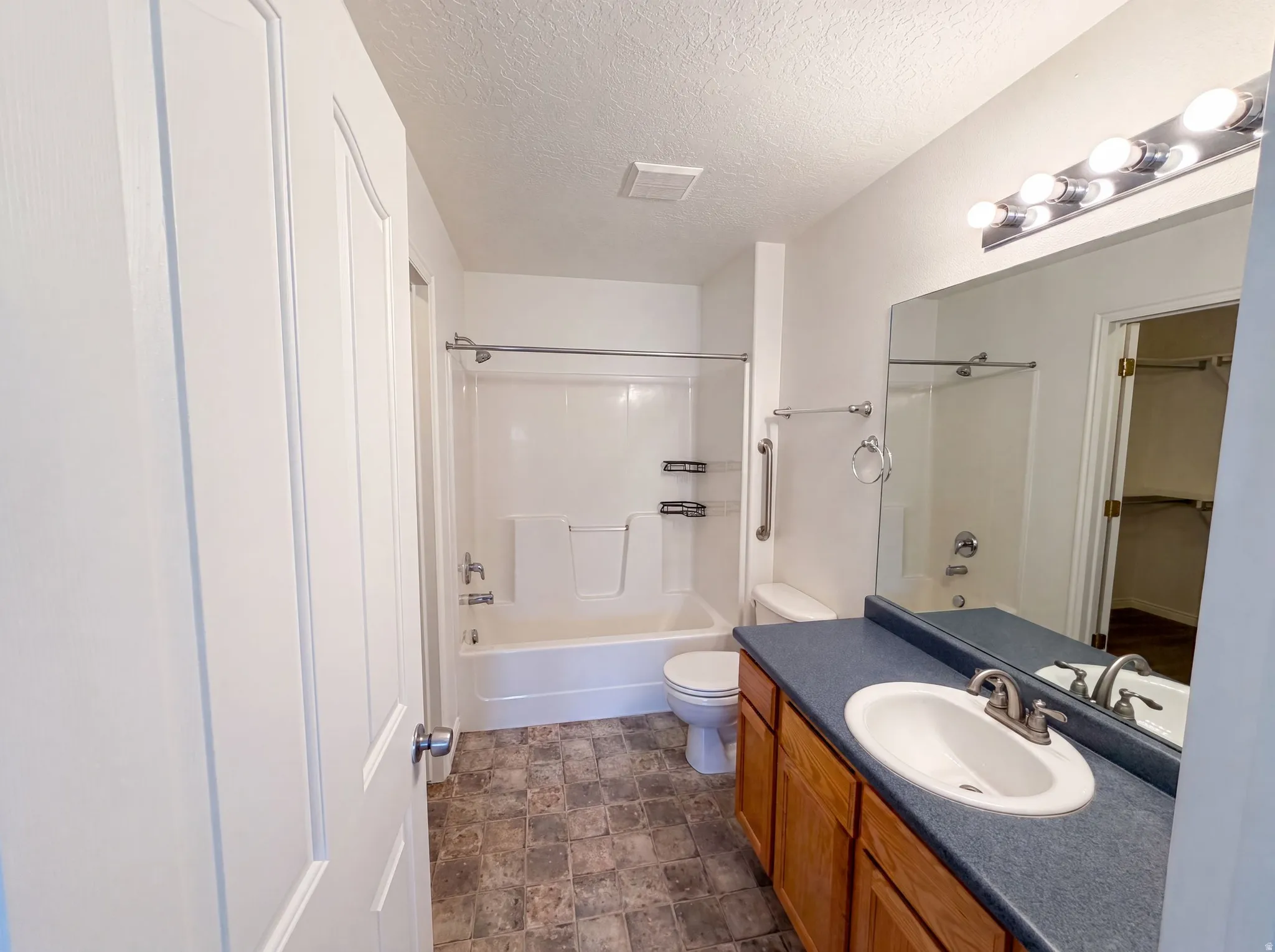 Full bathroom featuring a single vanity with wood-finish cabinetry, a white ceramic sink, a spacious mirror, and a combined shower-tub unit