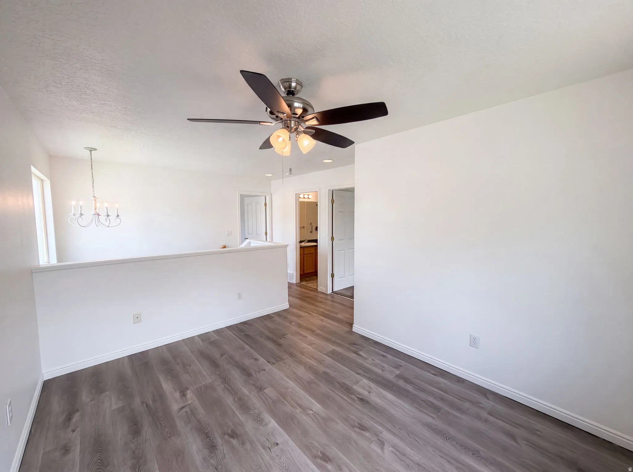 Wood-finish flooring throughout, featuring a ceiling fan with integrated lighting, a partial wall, and white trim