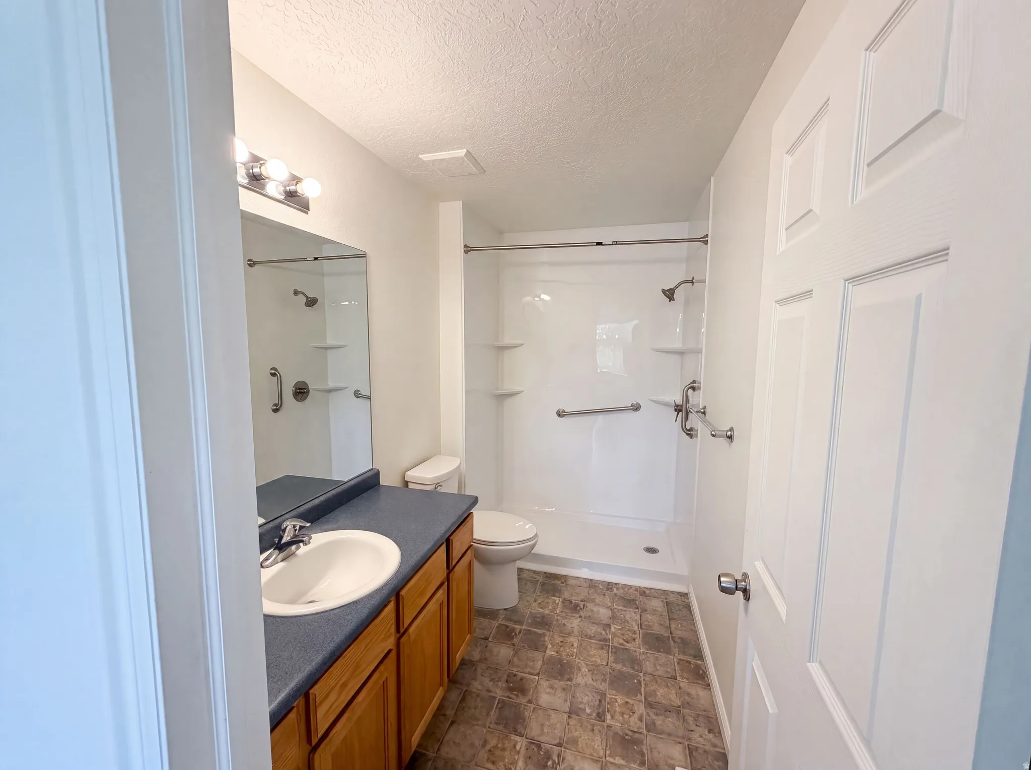 Full bathroom featuring a single vanity with wood cabinetry and a dark countertop, a white toilet, and a walk-in shower with grab bars