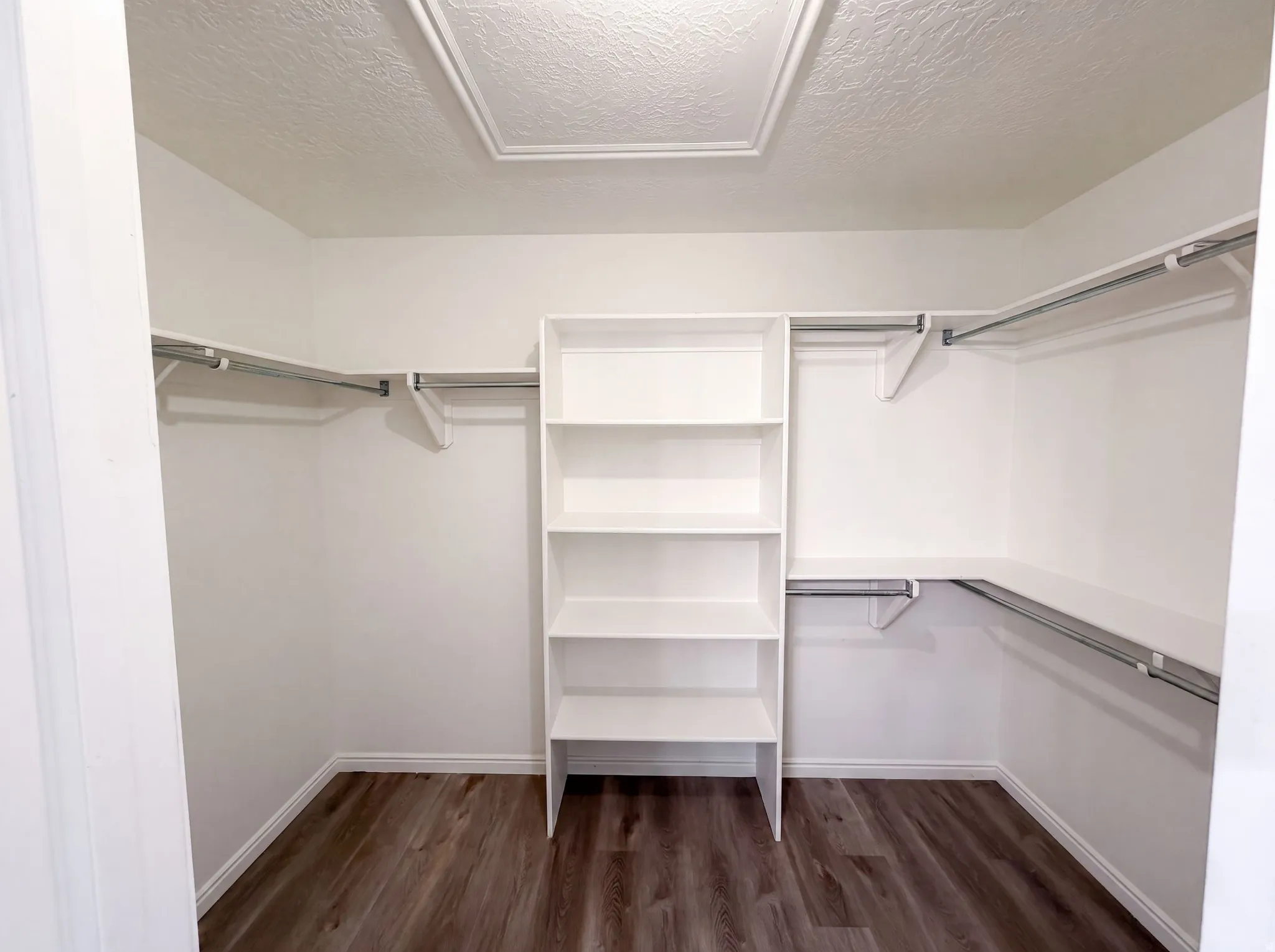 Walk-in closet featuring wood-finish flooring, white built-in shelving, multiple hanging rods, and perimeter shelving